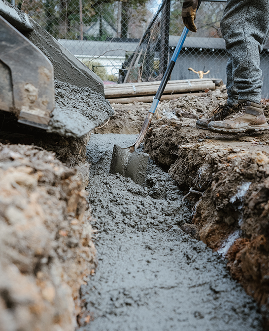 Worker Pouring Concrete Into Trench With Shovel